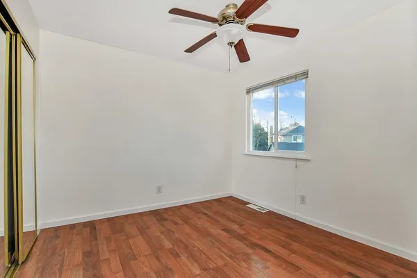 an empty room with wooden floor ceiling fan and windows