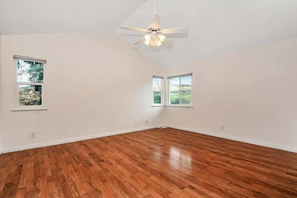 an empty room with wooden floor chandelier fan and windows