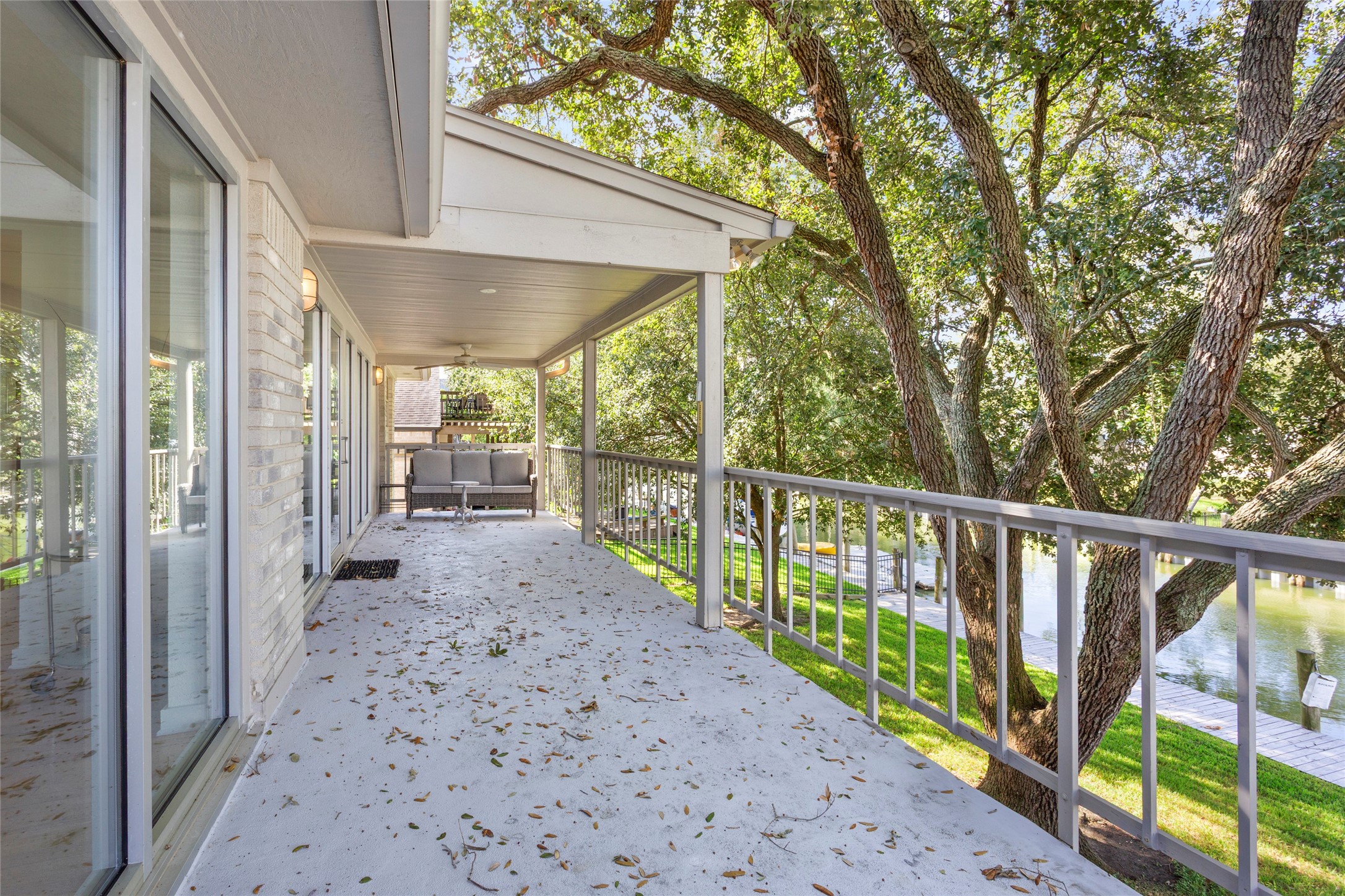 67 Harbor Lane Kemah, TX 77565 - Photo 23 of 47 This backyard upper area showcases a spacious, covered balcony overlooking a lush, tree-filled landscape with a view of the serene waterway. It features sliding glass doors, providing easy access to the interior, and ample space for outdoor seating, perfect for relaxation and enjoying nature.