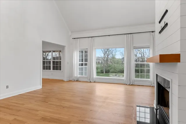 a view of an empty room with wooden floor and a kitchen