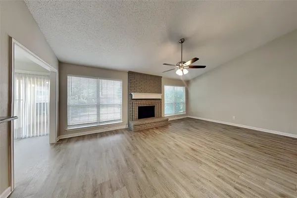 an empty room with wooden floor a ceiling fan and windows