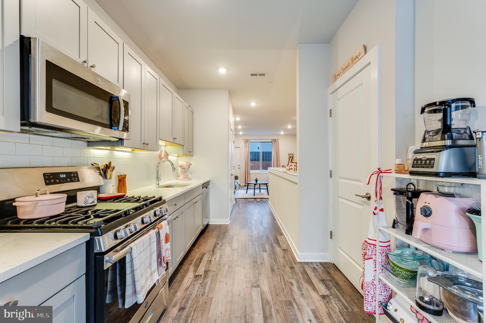 a kitchen with stainless steel appliances a stove top oven a sink a refrigerator white cabinets and wooden floor