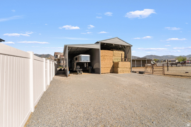 3678 Spiral Springs Road, Unit 204 Tooele, UT 84074 - Photo 50 of 59 Gravel driveway featuring a white privacy fence, an open-sided metal structure, and a fenced animal enclosure