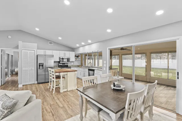 a open dining room with stainless steel appliances granite countertop a stove a refrigerator a couch with white cabinets and couches chairs with wooden floor