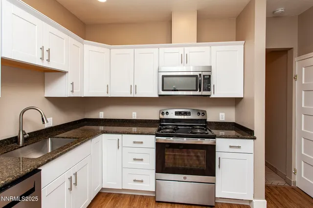 a white kitchen with granite countertop a stove and a sink