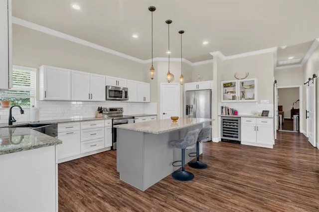 a large kitchen with stainless steel appliances kitchen island granite countertop a stove a sink a refrigerator and white cabinets with wooden floor