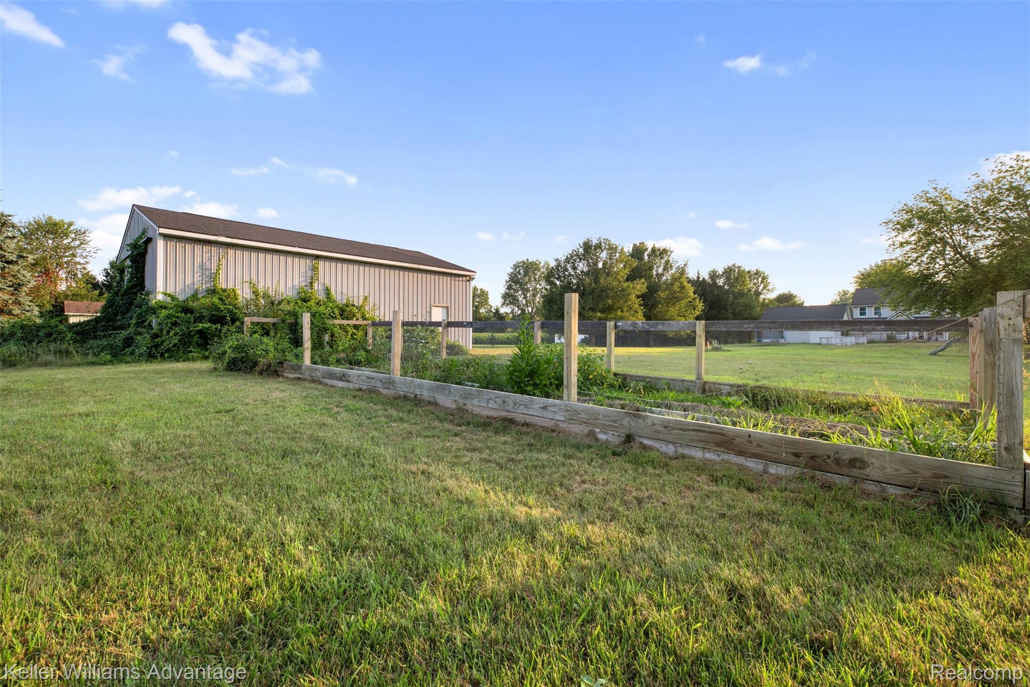 22627 Otter Road New Boston, MI 48164 - Photo 39 of 52 Expansive green lawn with a large, grey metal-sided outbuilding and a raised garden bed with wood borders