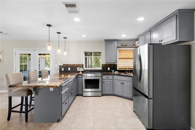a kitchen with stainless steel appliances granite countertop a stove a refrigerator a kitchen island a stove and a dining table with wooden floor