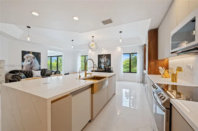 a large white kitchen with a stove a sink a refrigerator and a dining table view