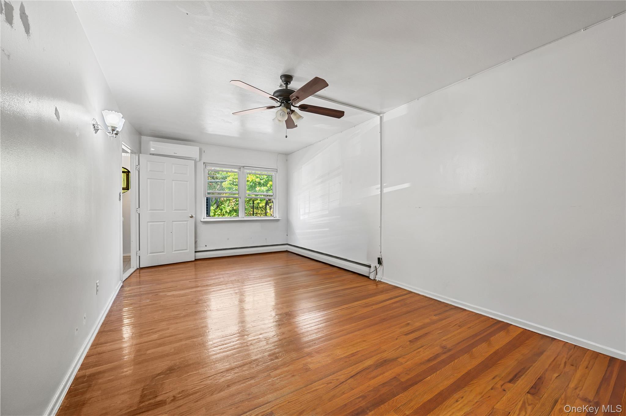152-10 Peck Avenue Queens, NY 11355 - Photo 11 of 26 Unfurnished room featuring hardwood / wood-style floors, ceiling fan, a baseboard radiator, and an AC wall unit