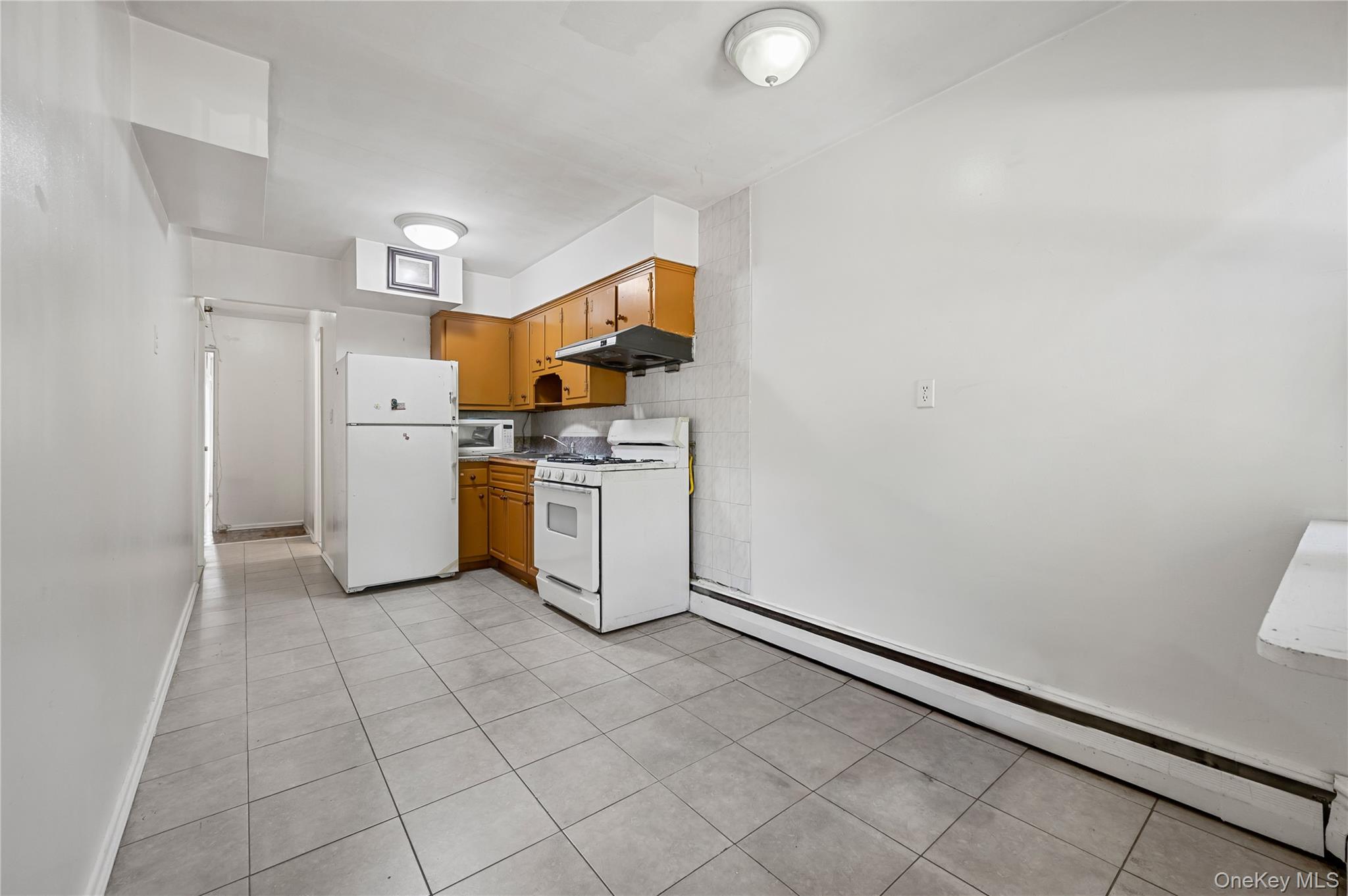 152-10 Peck Avenue Queens, NY 11355 - Photo 10 of 26 Kitchen with a baseboard radiator, white appliances, brown cabinetry, light countertops, and light tile patterned floors
