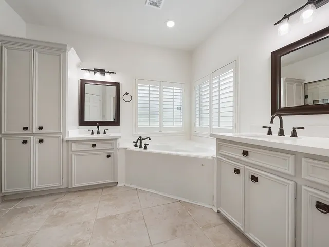a bathroom with double vanity sink a mirror a bathtub and window