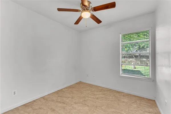 an empty room with chandelier fan and windows