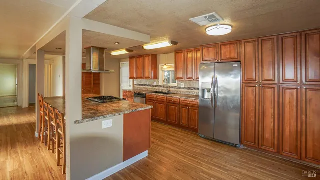 a kitchen with stainless steel appliances granite countertop a refrigerator a stove and a sink with wooden floor