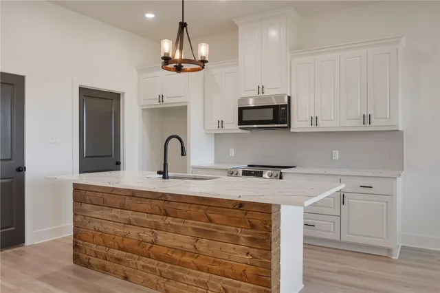 a large kitchen with kitchen island a stove a sink a refrigerator and white cabinets with wooden floor