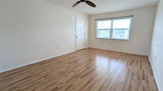 an empty room with wooden floor chandelier fan and windows