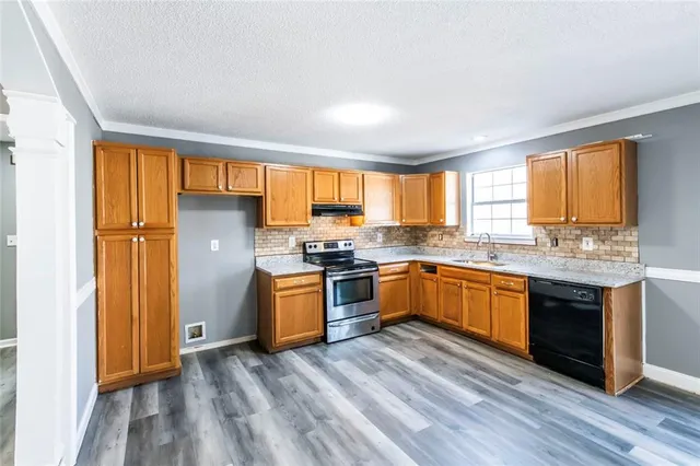 a kitchen with stainless steel appliances granite countertop a refrigerator a sink dishwasher a stove and white countertops with wooden floor