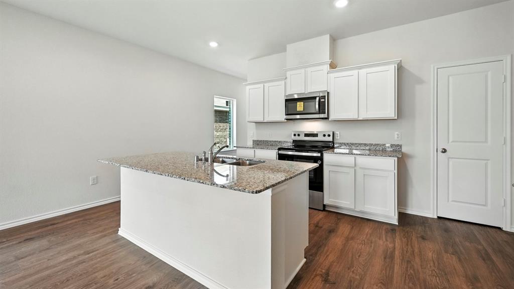 122 Pheasant Run Road Terrell, TX 75160 - Photo 29 of 36 Kitchen featuring a central island with a built-in sink, light speckled countertops, white cabinetry, stainless steel appliances, and wood-finish flooring