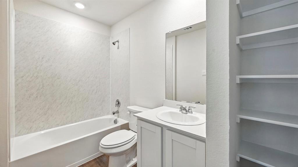 122 Pheasant Run Road Terrell, TX 75160 - Photo 4 of 36 Bathroom featuring a white bathtub with a textured surround, a vanity with a white countertop and integrated sink, a large mirror, and built-in shelving