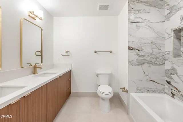 a bathroom with a granite countertop sink a toilet a mirror and bathtub