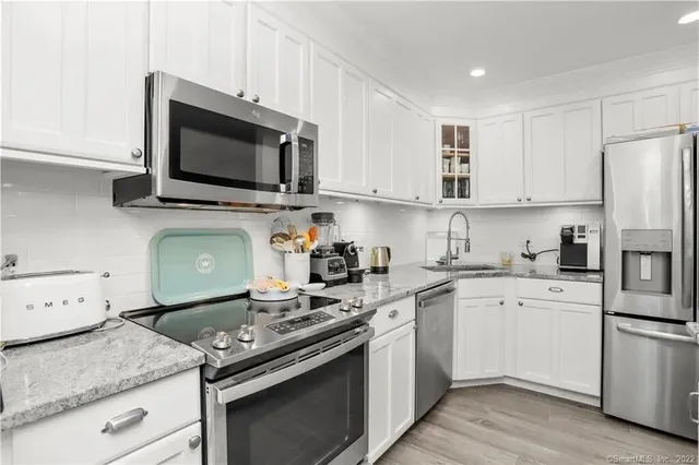 a kitchen with stainless steel appliances granite countertop a stove top oven a sink dishwasher and a refrigerator with wooden cabinets