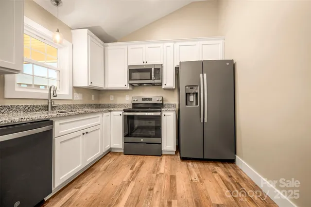 a kitchen with stainless steel appliances granite countertop a refrigerator a sink dishwasher a stove top oven a refrigerator with white cabinets and wooden floor