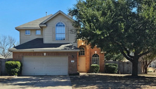 Traditional-style home featuring a garage, driveway, brick siding, and roof with shingles