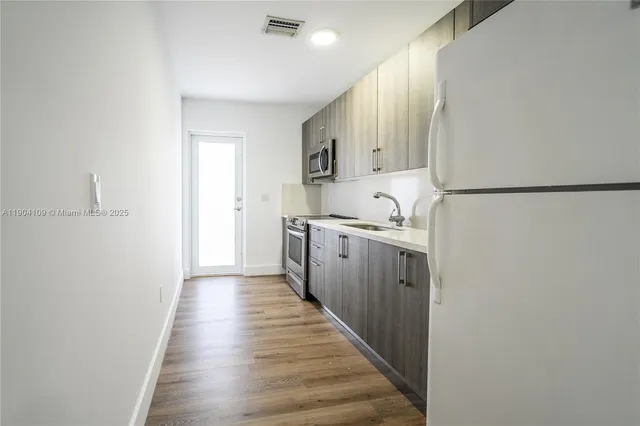 a kitchen with a sink a refrigerator and wooden floor