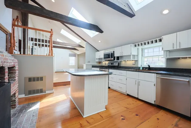 a kitchen with stainless steel appliances granite countertop a refrigerator a sink dishwasher a stove and white cabinets with wooden floor