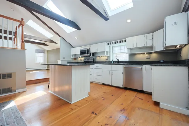 a kitchen with stainless steel appliances granite countertop a stove top oven a sink dishwasher and white cabinets with wooden floor