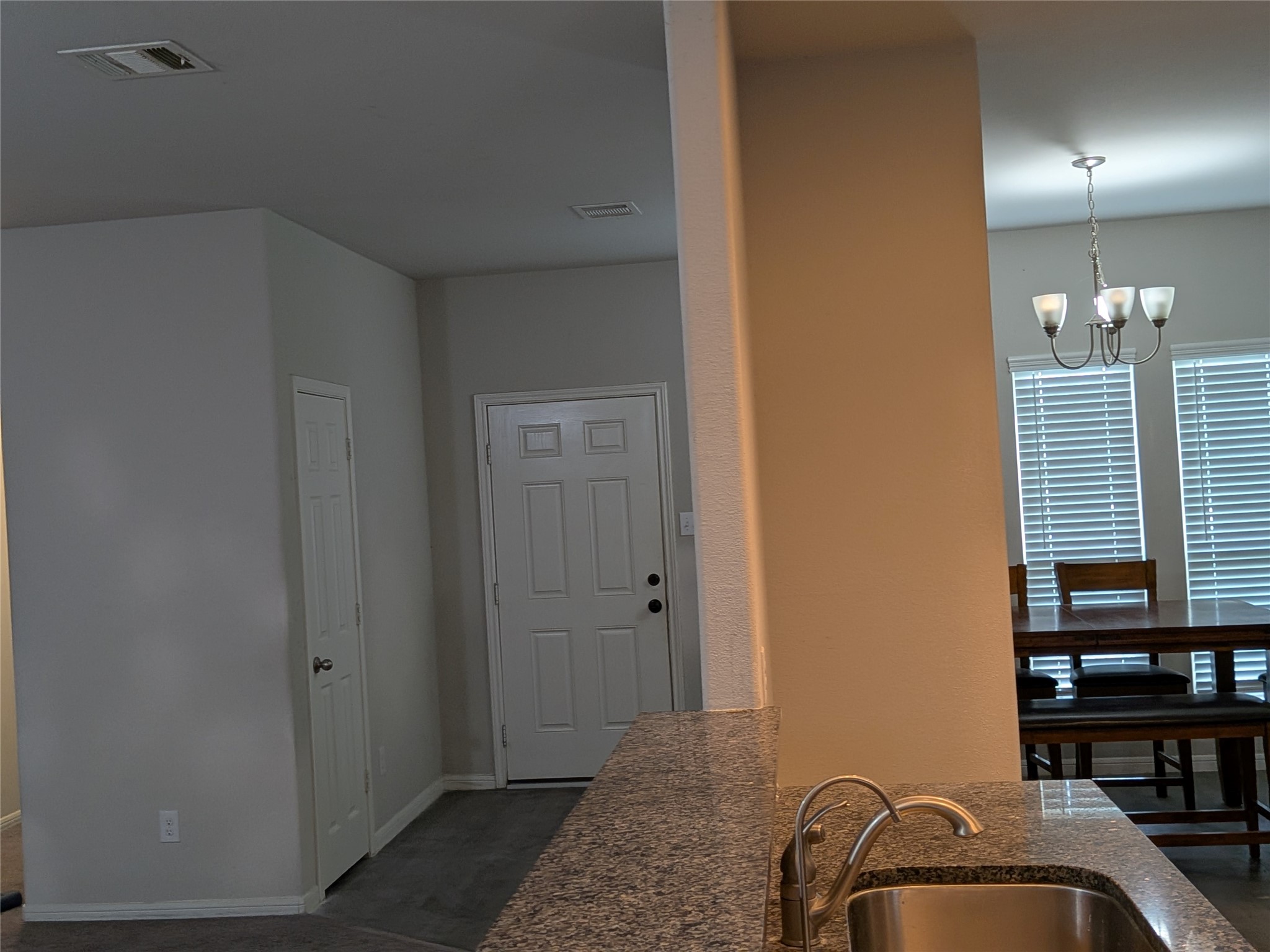 15730 Joe Dimaggio Street Splendora, TX 77372 - Photo 5 of 20 This photo showcases a modern entryway with a view into the dining area. It features a granite countertop with a sink, a ceiling light fixture in the dining room, and neutral-colored walls for a warm and inviting atmosphere.