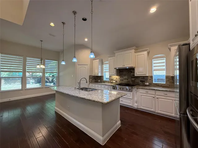 a large kitchen with granite countertop a stove a sink a refrigerator and a granite countertops with wooden floor