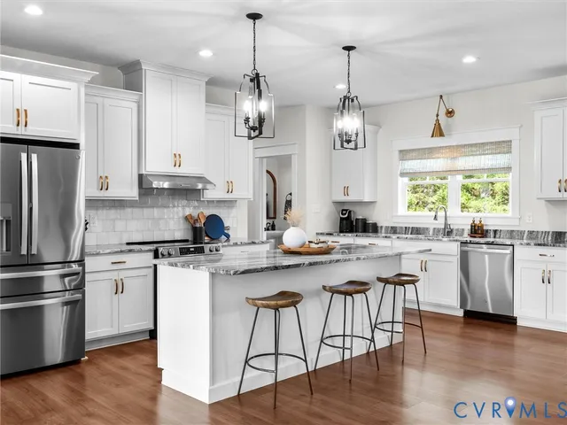 a kitchen with stainless steel appliances granite countertop a sink a stove a refrigerator and island with wooden floor