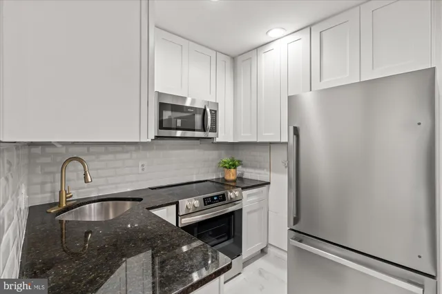 a kitchen with stainless steel appliances granite countertop a refrigerator a sink a stove and white cabinets