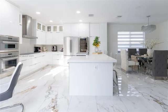 a kitchen with stainless steel appliances kitchen island granite countertop a stove a sink a oven a dining table and chairs with white cabinets