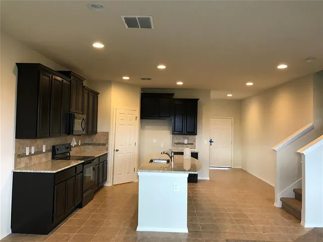 a large kitchen with stainless steel appliances a large counter top a stove a sink dishwasher and a refrigerator with wooden floor