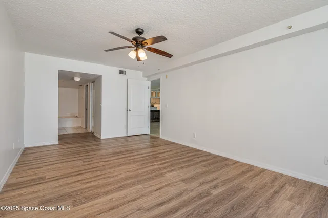 a view of an empty room with wooden floor and a ceiling fan