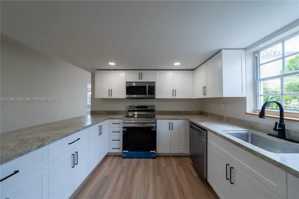 a kitchen with stainless steel appliances granite countertop white cabinets a sink dishwasher a stove and a refrigerator with wooden floor