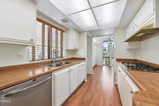 a kitchen with stainless steel appliances a sink dishwasher a stove and white cabinets with wooden floor