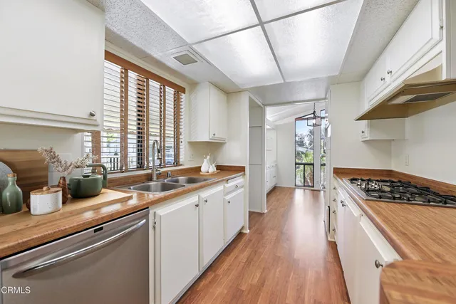 a kitchen with stainless steel appliances granite countertop a stove a sink dishwasher and white cabinets with wooden floor