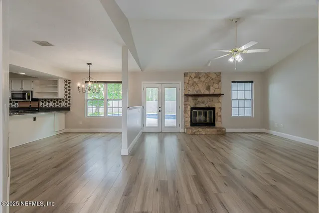an empty room with wooden floor fireplace and windows