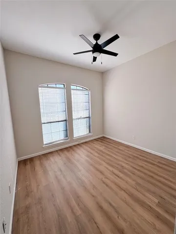 an empty room with wooden floor fan and windows