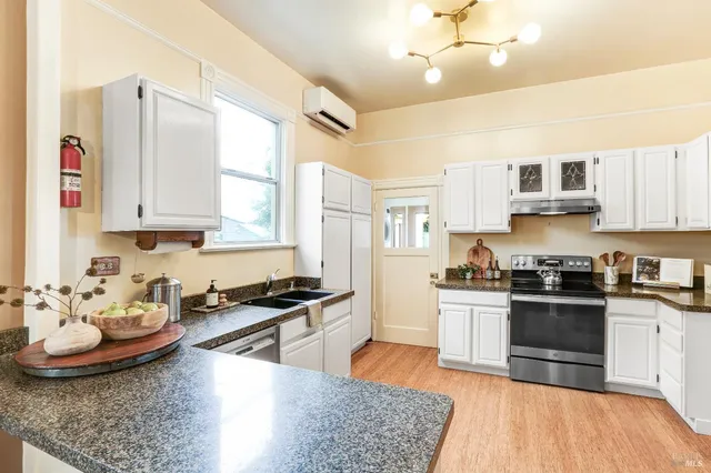 a kitchen with stainless steel appliances kitchen island granite countertop a sink dishwasher stove and white cabinets with wooden floor