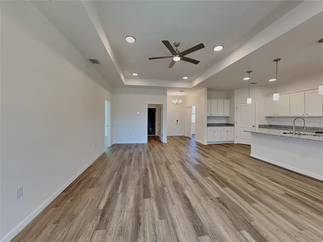 a view of an empty room and kitchen view with wooden floor