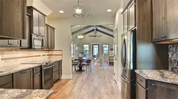 a kitchen with stainless steel appliances granite countertop a refrigerator a sink dishwasher a stove and a dining table with wooden floor