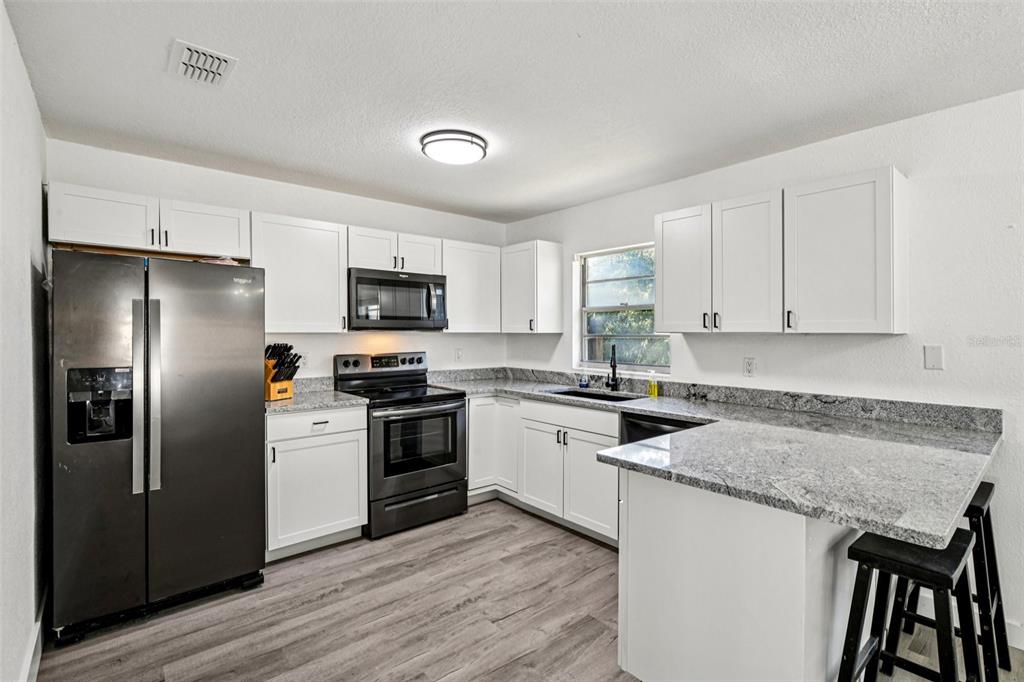 56305 Redbud Road Astor, FL 32102 - Photo 14 of 32 a kitchen with granite countertop a refrigerator a sink a stove a microwave and wooden floor