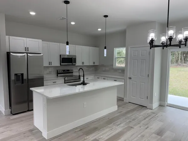 a large kitchen with granite countertop a refrigerator a oven a stove and a wooden floor