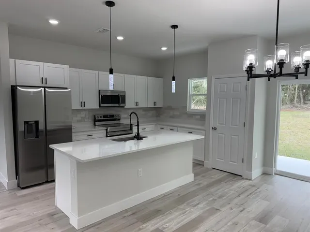 a large kitchen with granite countertop a refrigerator a oven a stove and a wooden floor