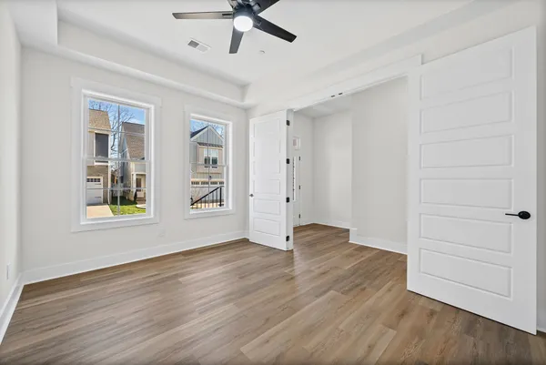 an empty room with wooden floor chandelier fan and windows