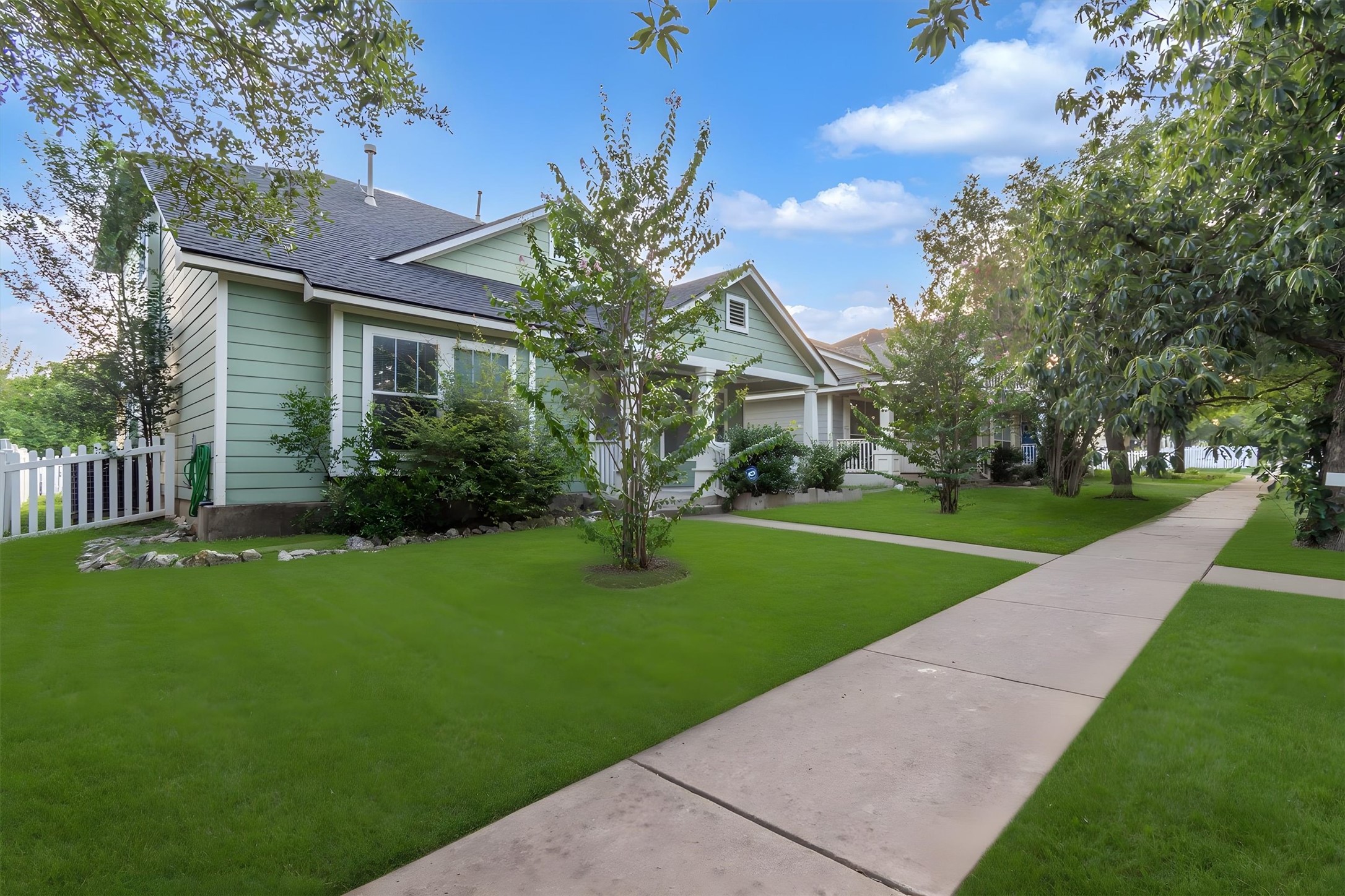 A neatly maintained lawn and sidewalk lead to a charming light green residence with a welcoming front porch.